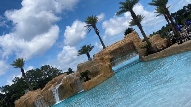 A swimming pool with clear blue water, palm trees, and a waterfall feature. - The Wharf resort Orange Beach with Waterpark included (Orange Beach)