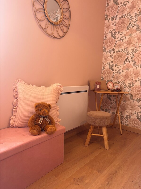 A cozy room with a pink sofa, a teddy bear, a small wooden stool, a mirror, and a floral wallpaper. - Gîte le Cottage Demmy Rose (Commes)