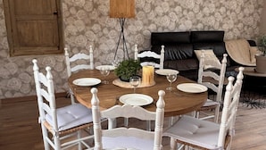 A dining area with a round wooden table, white chairs, and a floral wallpaper background.