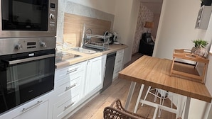 A modern kitchen with white cabinets, a built-in oven, a microwave, and a wooden dining table with two wicker chairs.