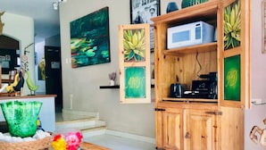 A living room with a wooden cabinet, a glass table with decorative items, a painting of a pond, and a microwave on the cabinet. - 38 Pax 4 Connected Pool Villas (Playa del Carmen)