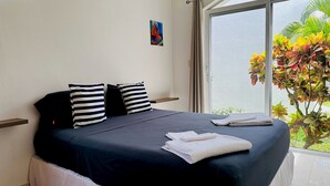 Un dormitorio con cama, almohadas y ventana con vistas a plantas.