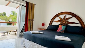 Un dormitorio con cama, una mesita de noche, una ventana con cortinas y vistas al exterior con vegetación.
