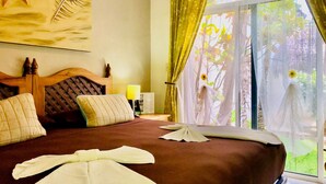 A hotel room with a large bed, a wooden headboard, a painting of a star and a shell, a nightstand with a lamp, and a view of greenery through the window. - 30 Pax 3 Connected Pool Villas (Playa del Carmen)