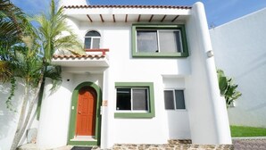 Un edificio de dos pisos con fachada blanca, marcos de ventana verdes y una puerta roja.