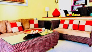 Una sala de estar con un conjunto de sofás, una mesa de centro y un comedor con un jarrón rojo y una exposición de frutas.