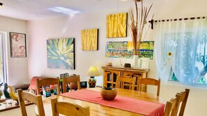 A dining area with a wooden table, chairs, and a red tablecloth. There are paintings on the walls, a lamp, and a window with curtains. - 22 Pax 2 Connected Pool Villas (Playa del Carmen)