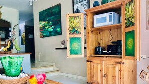 A living room with a wooden cabinet, a glass table with decorative items, a painting of a pond, and a microwave on the cabinet. - 22 Pax 2 Connected Pool Villas (Playa del Carmen)