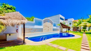 A swimming pool with a thatched roof structure, a stone wall, and a clear blue sky. - 8 Pax Basic Pool Villa (Playa del Carmen)