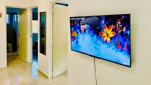 Un pasillo con un televisor reproduciendo música de flauta budista, una estatua de Buda y tres formas de luna creciente de madera en la pared.