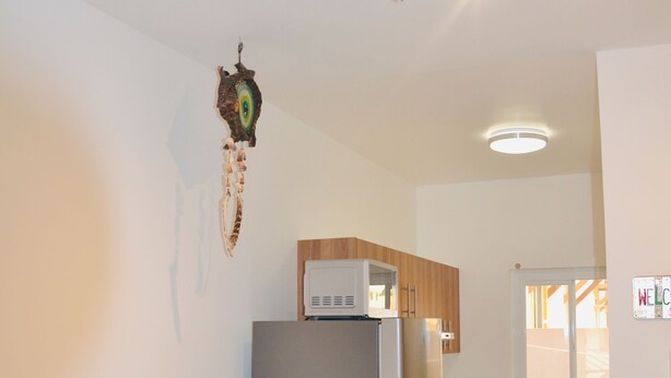 Una cocina moderna con refrigerador, microondas y armarios de madera. Se aprecia una mesa de comedor con sillas y una lámpara fijada a la pared.
