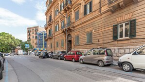 Eine Straße mit parkenden Autos und einem Gebäude mit zahlreichen Fenstern und Balkonen.