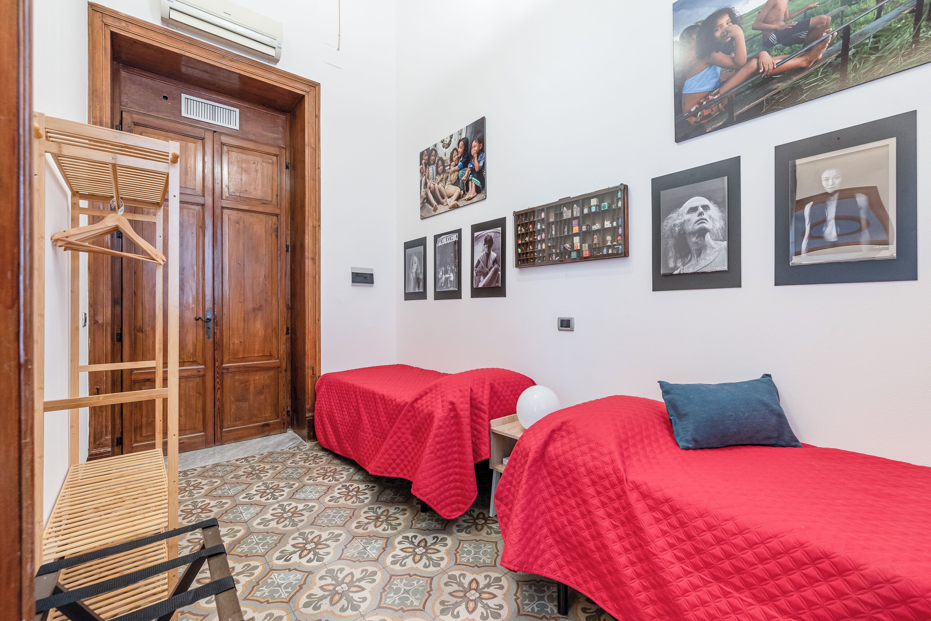 A room with two beds, a wooden wardrobe, and a wall with framed pictures.
