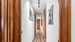 Ein Korridor mit Holzboden und Türen, der zu einem Raum mit Holztür und einer Deckenleuchte führt.