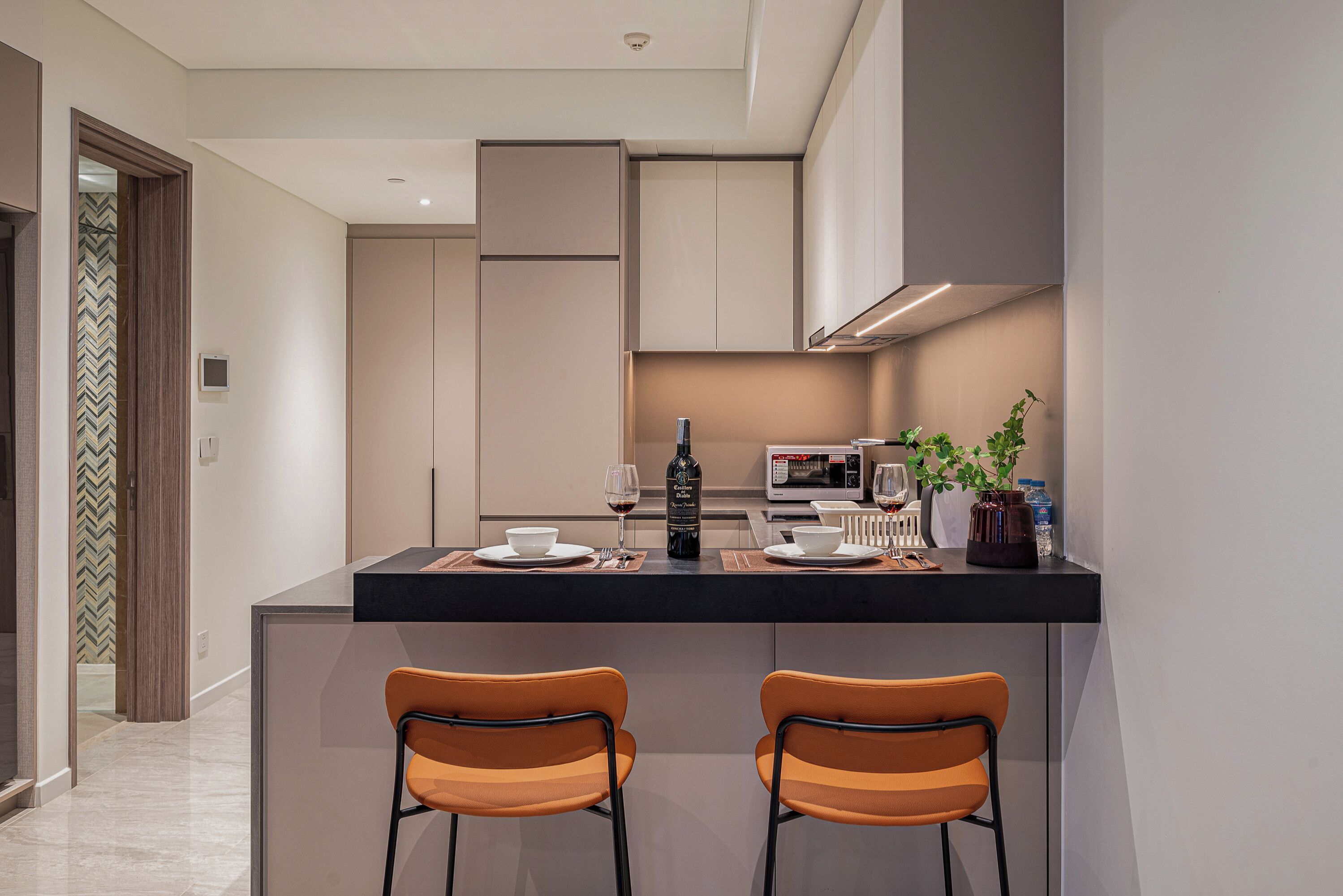 A modern kitchen with a central island, two bar stools, a microwave, and a potted plant.