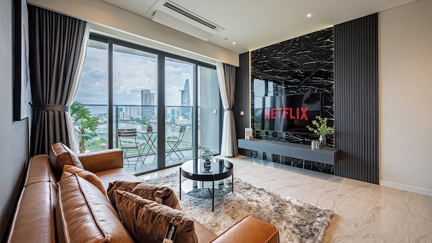 A modern living room with a leather sofa, a glass coffee table, and a large window offering a city view. - The Opera Residences (Ho Chi Minh City)