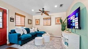 A living room with a blue sofa, a white coffee table, a ceiling fan, and a flat-screen TV mounted on the wall. - MB Oceanviews and Rooftop Deck 2BR w/ Parking (San Diego)