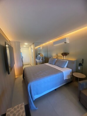 A modern hotel room with a large bed, bedside tables, a small round table, and a mirror.