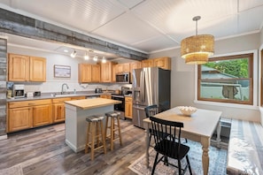 A modern kitchen with wooden cabinets, stainless steel appliances, and a large island with stools. - Walk to downtown + lake  (Boyne City)