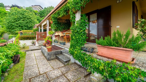 Una casa con porche cubierto, escalones de piedra y plantas en macetas.