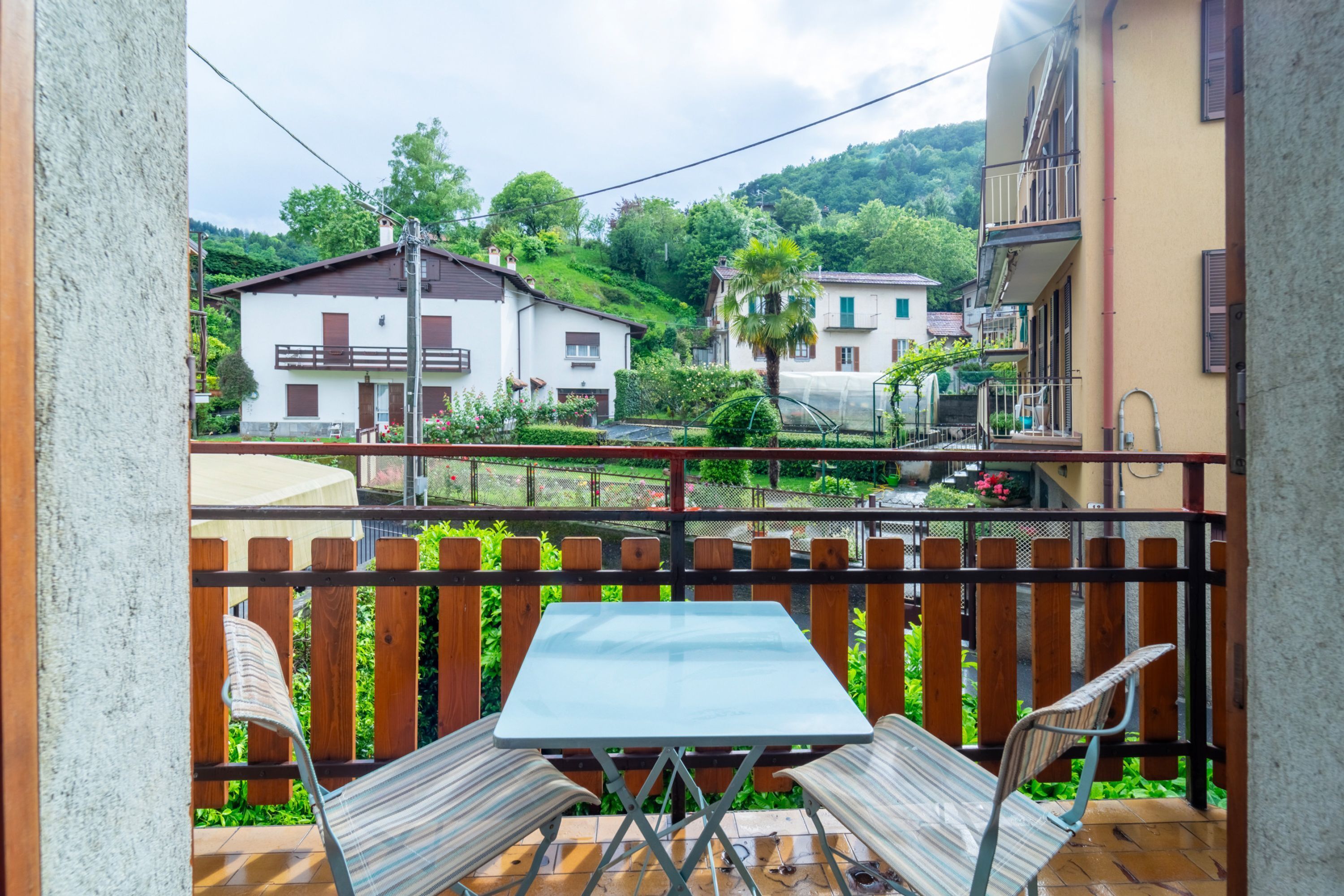Un balcón con mesa y sillas, con vista a una zona residencial con casas y vegetación.
