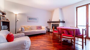 Una sala de estar con sofá, una mesa de comedor con sillas, una chimenea y una estantería.