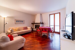 Un salon comprenant un canapé, une table à manger avec des chaises, une cheminée et un téléviseur.
