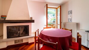 Comedor con una mesa redonda cubierta con mantel rojo, sillas de madera, chimenea y vistas al exterior.