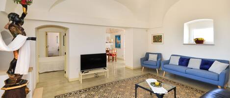 A living room with a blue sofa, a black leather couch, a TV on a stand, a decorative statue, and a patterned rug.