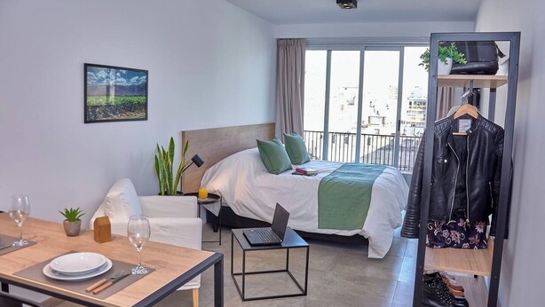 A hotel room with a bed, a desk, a chair, a dining table, and a balcony with a view of the city. - Céntrico Studio Para 2 Personas (Buenos Aires)