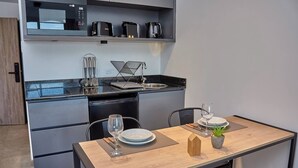 A modern kitchen with a microwave, toaster, and coffee maker on the countertop. There is a dining table with a plant and a wine glass. - Céntrico Studio Para 2 Personas (Buenos Aires)