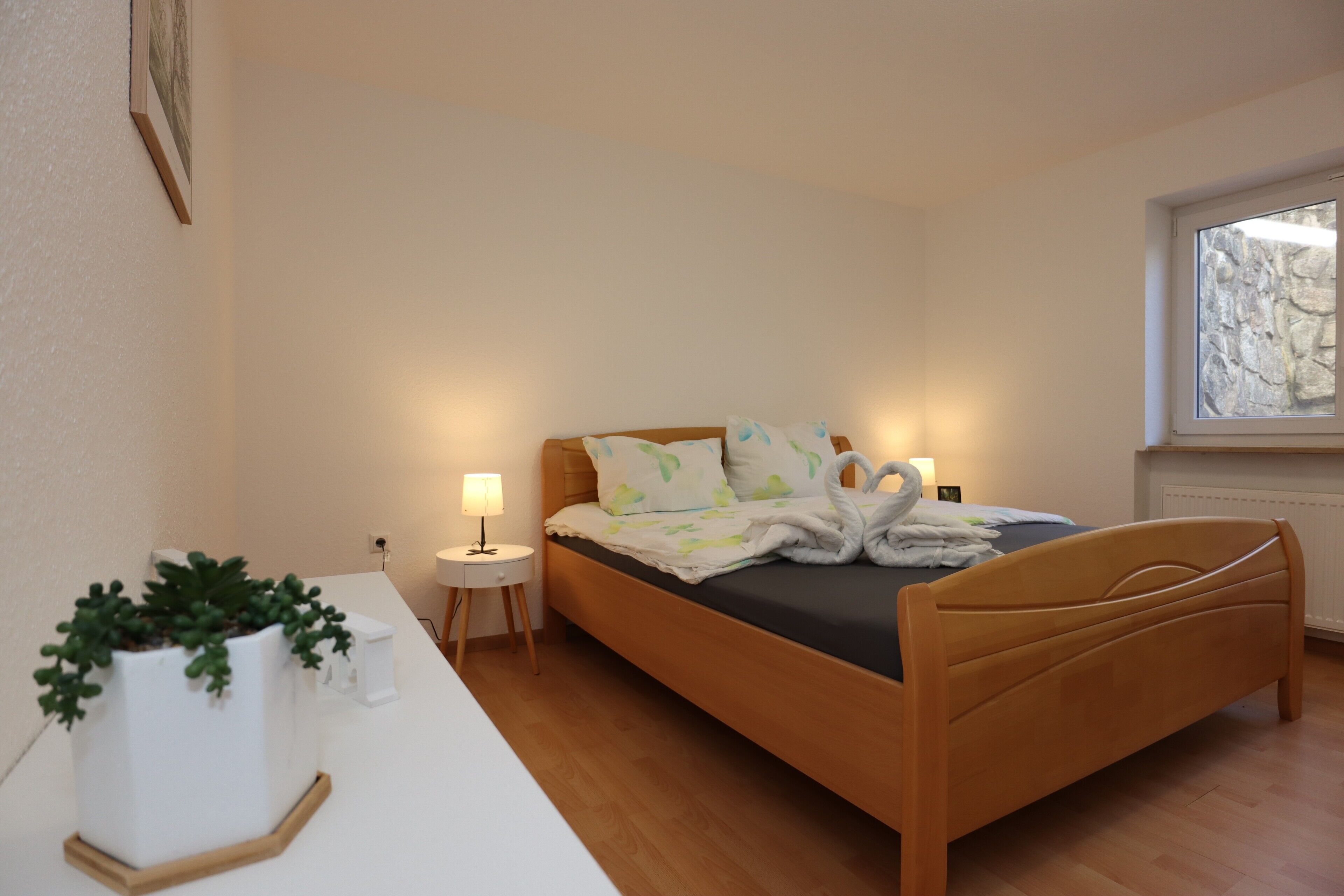 Ein Schlafzimmer mit einem hölzernen Bett, einem Nachttisch mit Lampe und einer Topfpflanze.