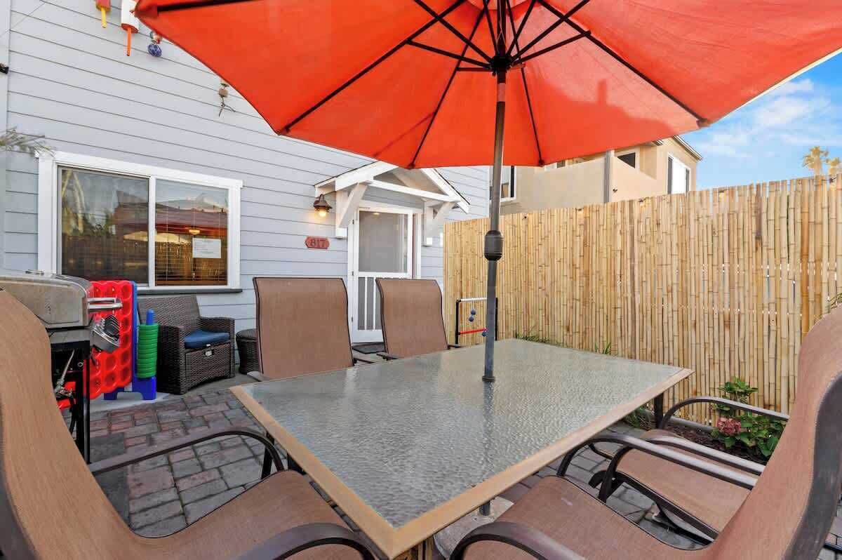 Eine Terrasse im Freien mit Tisch und Stühlen, einem roten Sonnenschirm und einem Holzzaun.