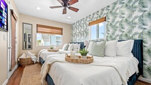 A bedroom with a bed, a ceiling fan, a window, and a wall with a leaf pattern.