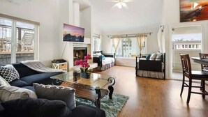 A spacious living area with a fireplace, a sofa, a dining table, and a ceiling fan.