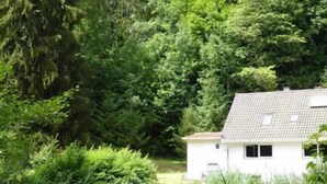 A chair in a grassy area with dense foliage and a white building in the background. - Vacation home time out from everyday life (Kirchenkirnberg)