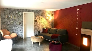 A living room with a stone wall, a red accent wall, a sofa, a coffee table, and a chair. - Vacation home time out from everyday life (Kirchenkirnberg)