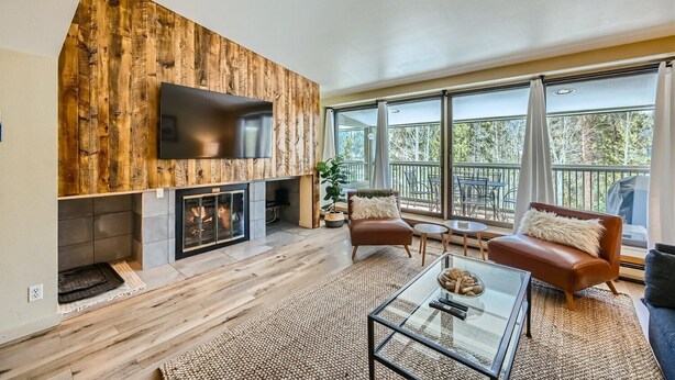 A modern living room with a fireplace, leather sofas, a glass coffee table, and a large window overlooking a balcony. - Modern Mountain Getaway with Stunning Views (Keystone)