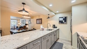 A modern kitchen with granite countertops, a large island, and a dining area visible through an open door. - Modern Mountain Getaway with Stunning Views (Keystone)