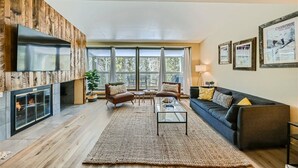 A modern living room with a fireplace, comfortable seating, and large windows offering a view of the outdoors. - Modern Mountain Getaway with Stunning Views (Keystone)