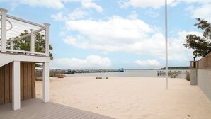 Une terrasse en bois qui mène à une plage de sable, avec une jetée en arrière-plan.