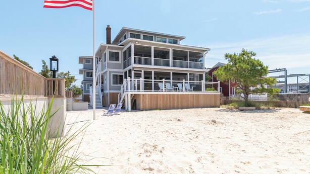 Une propriété en bord de mer, composée de plusieurs étages, dotée d’un balcon, d’un drapeau et d’une clôture en bois.