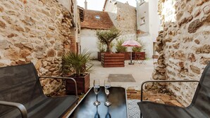 Un patio estrecho con muros de piedra, una mesa de madera con dos vasos y asientos exteriores.