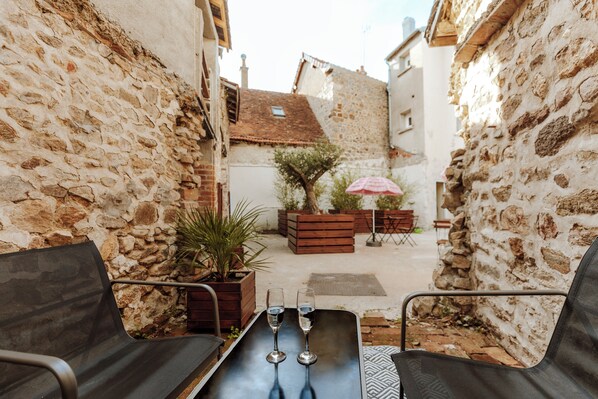 Un patio estrecho con muros de piedra, una mesa de madera con dos vasos y asientos exteriores.