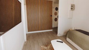 Habitación de hotel moderna con un separador de listones de madera, una cama con cubierta verde, una mesa blanca y un control remoto encima.