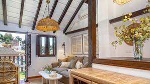 A cozy living room with a wooden table, wicker chair, and a sofa with cushions.
