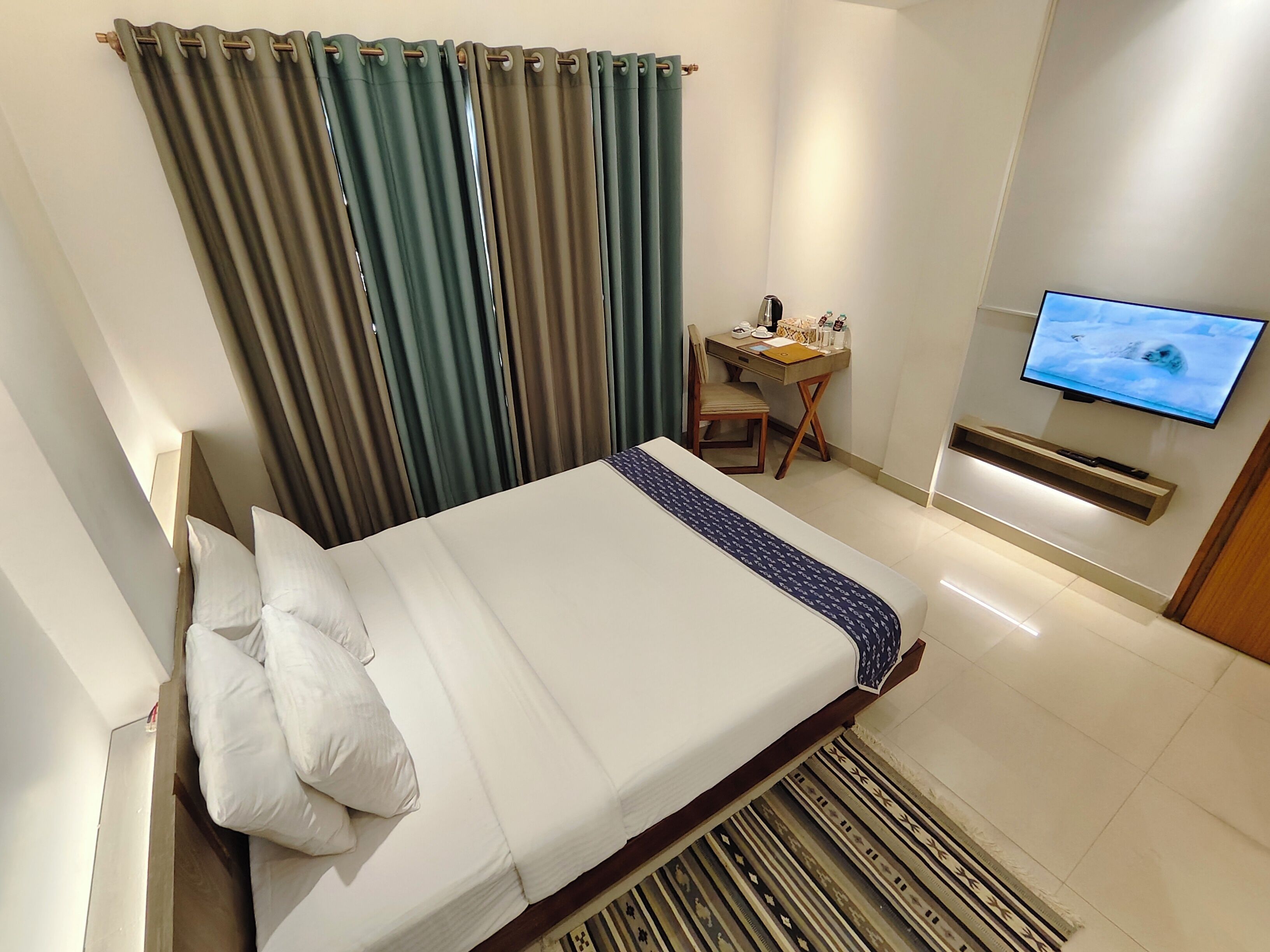 A hotel room with a bed, a desk, a chair, a television, and curtains.