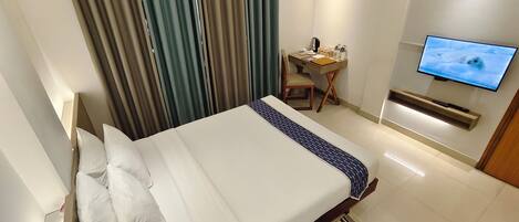 A hotel room with a bed, a desk, a chair, a television, and curtains.