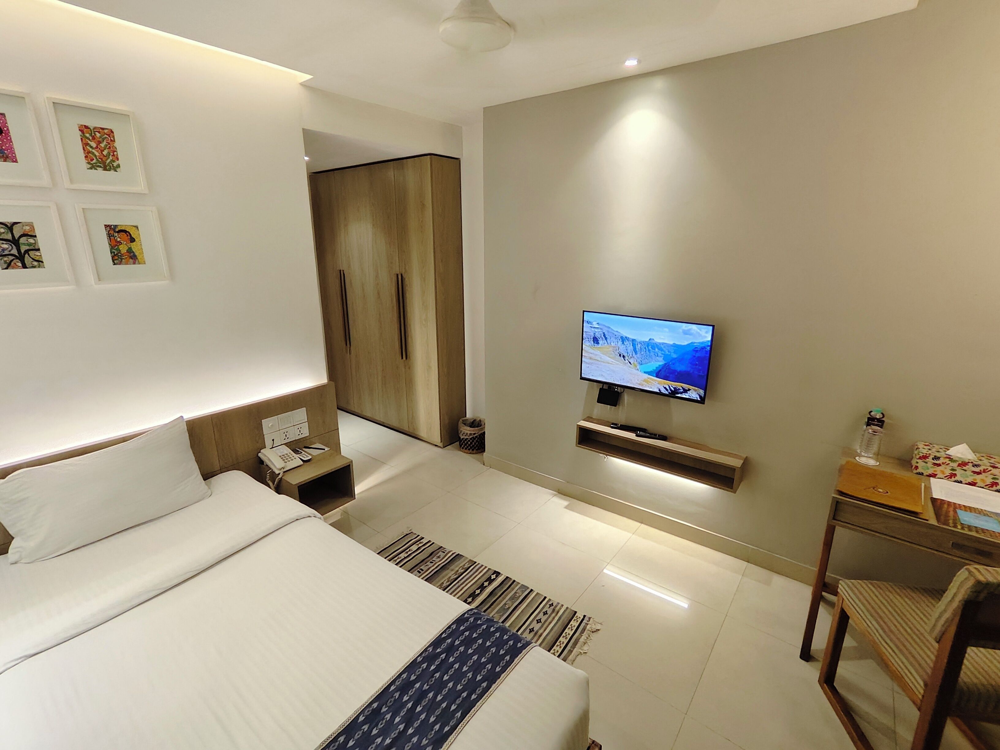 A modern hotel room with a large bed, a TV mounted on the wall, a desk with a chair, and a wardrobe.