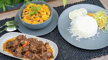 Een tafel met een kom curry, een bord rijst en een schotel vlees.